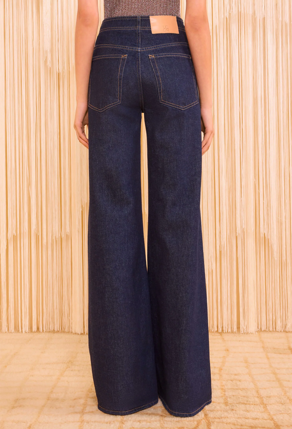 the back of a woman wearing dark blue jeans with a seam down the middle of the leg. textured beige background