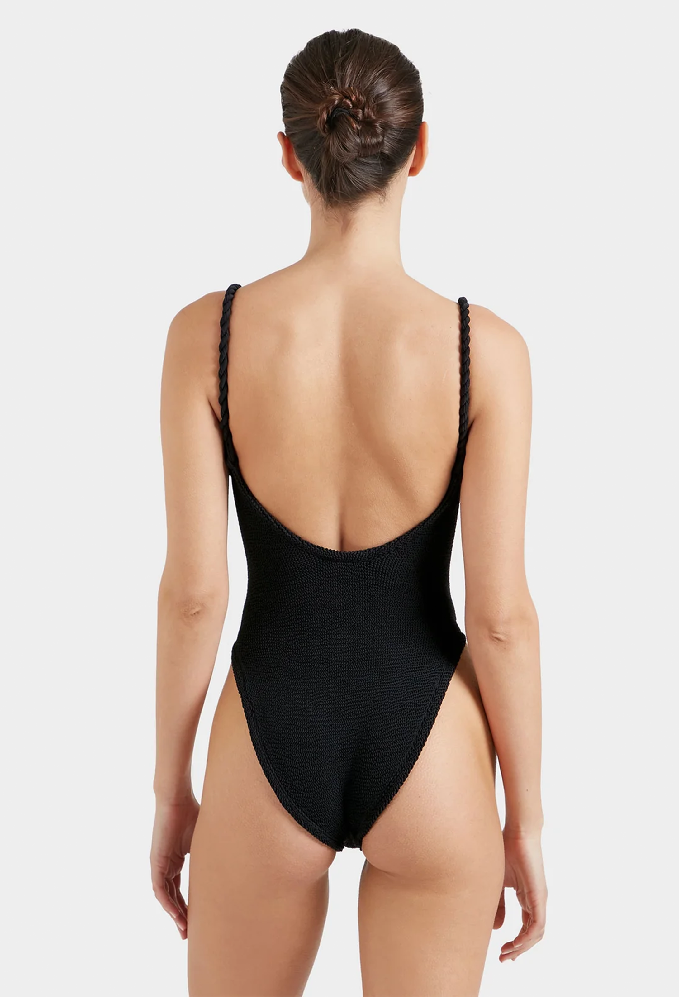 the back of a woman wearing a black one-piece swimsuit with rope braid straps. white background.