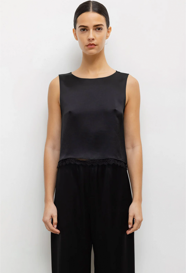 a woman wearing a black sleeveless cropped top with a lace hem and black pants. white background.