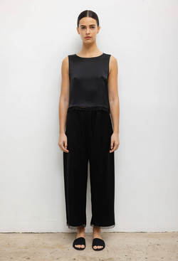 a woman wearing a black sleeveless top and black pants with a lace hem. white background.