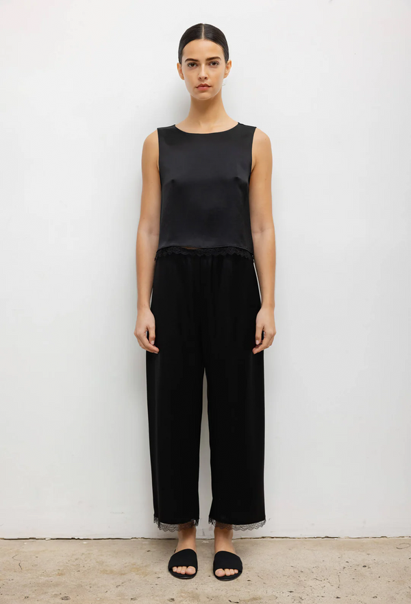 a woman wearing a black sleeveless top and black pants with a lace hem. white background.