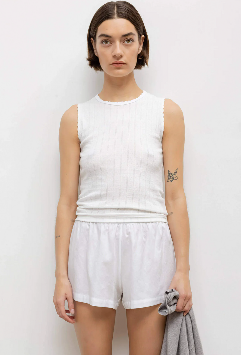 a woman wearing a white sleeveless pointelle cropped shirt and white shorts. white background.