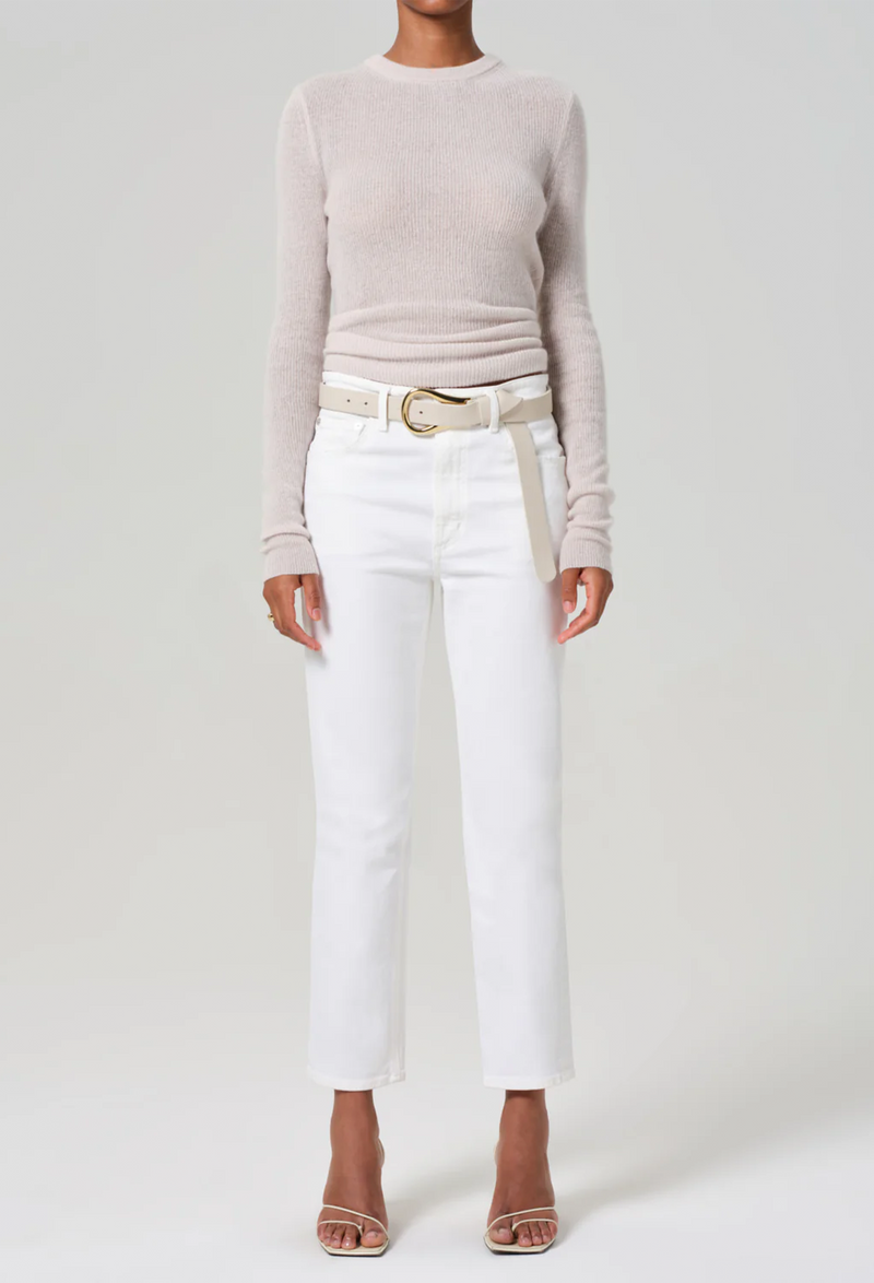 a woman wearing a sweater and slim straight leg white jeans cropped at the ankle. white background.