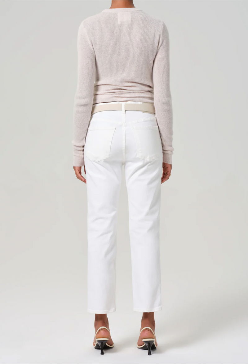 the back of a woman wearing a sweater and slim straight leg white jeans cropped at the ankle. white background.