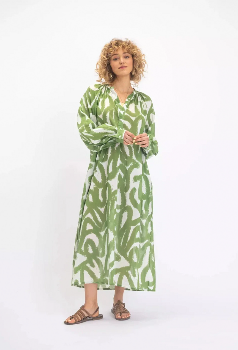a woman wearing a white midi long sleeve button v-neck dress with a green scribble design. white background.