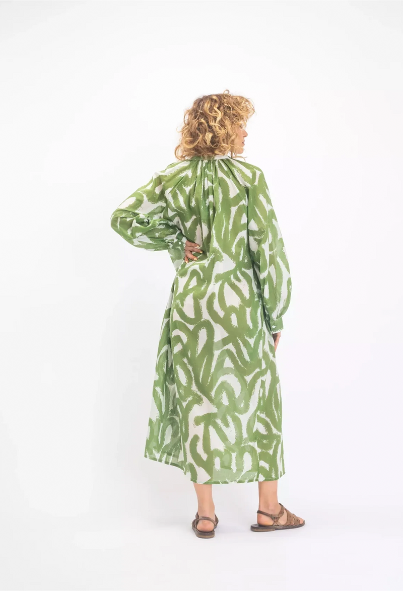 the back of a woman wearing a white midi long sleeve button v-neck dress with a green scribble design. white background.