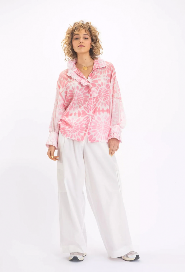 a woman wearing a white blouse with a pink floral print and a ruffled neck and sleeves. white background.