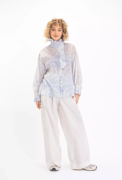 a woman wearing a white blouse with a blue floral print and a ruffled neck and sleeves. white background.
