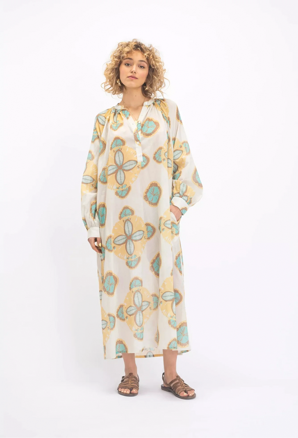 a woman wearing a long sleeve white button up v-neck dress with a blue and yellow circular design. white background.
