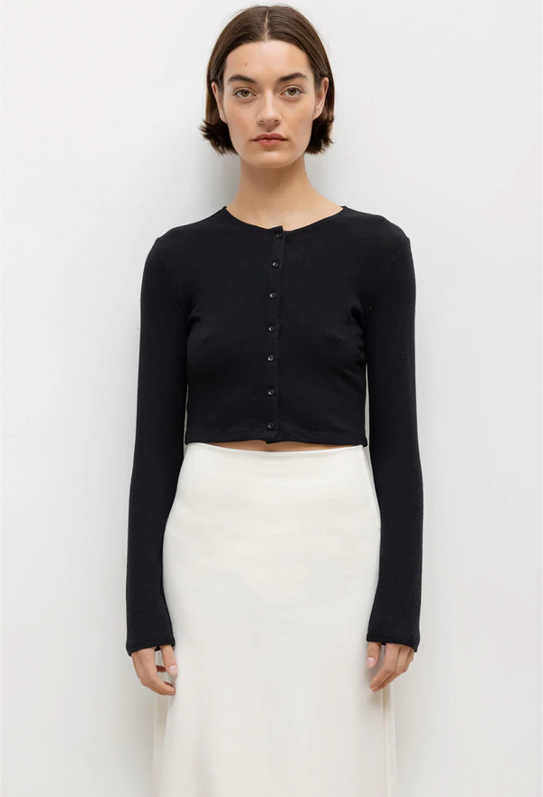 a woman wearing a black long sleeve cropped cardigan with black buttons and a white skirt. white background.