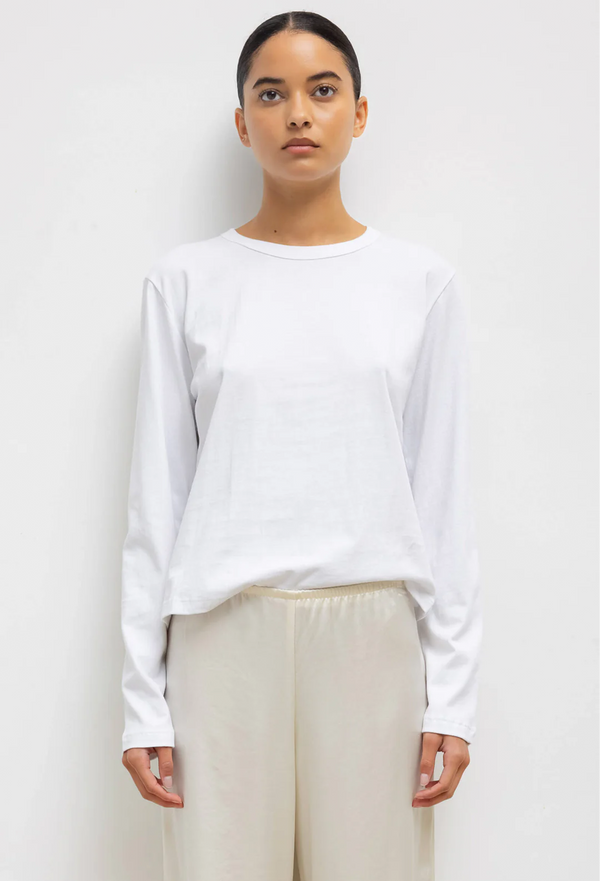 a woman wearing a white long sleeve t-shirt and champange pants. white background.