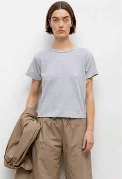 a woman wearing a heather grey t-shirt and beige pants. white background.