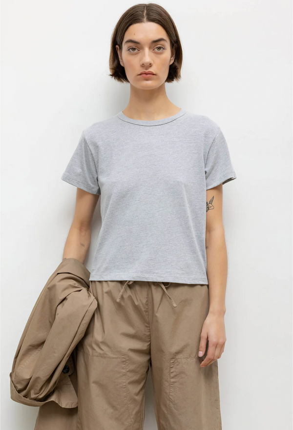a woman wearing a heather grey t-shirt and beige pants. white background.