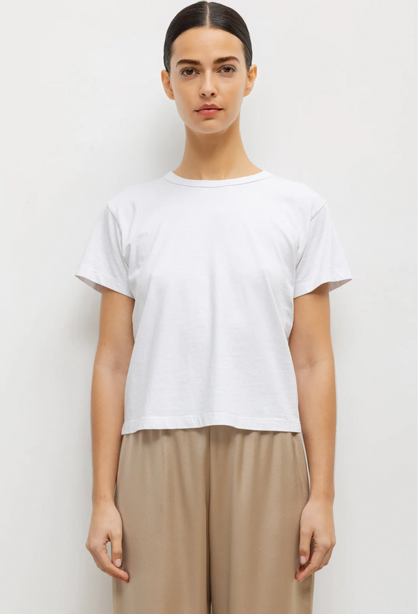 a woman wearing a white t-shirt and beige pants. white background.