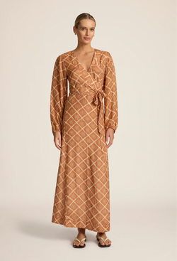 a woman wearing a rust brown maxi long sleeve wrap dress with a geometric sun print. white background.