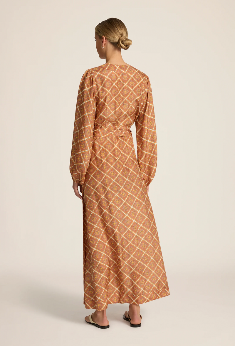 the back of a woman wearing a rust brown maxi long sleeve wrap dress with a geometric sun print. white background.