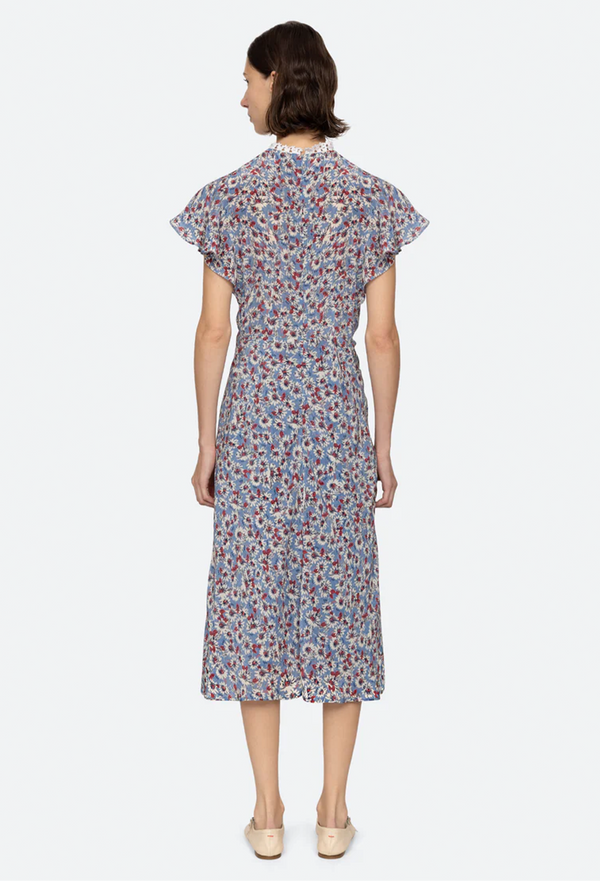the back of a woman wearing a blue high neck midi dress with short flutter sleeves and a white and red floral print. white background.