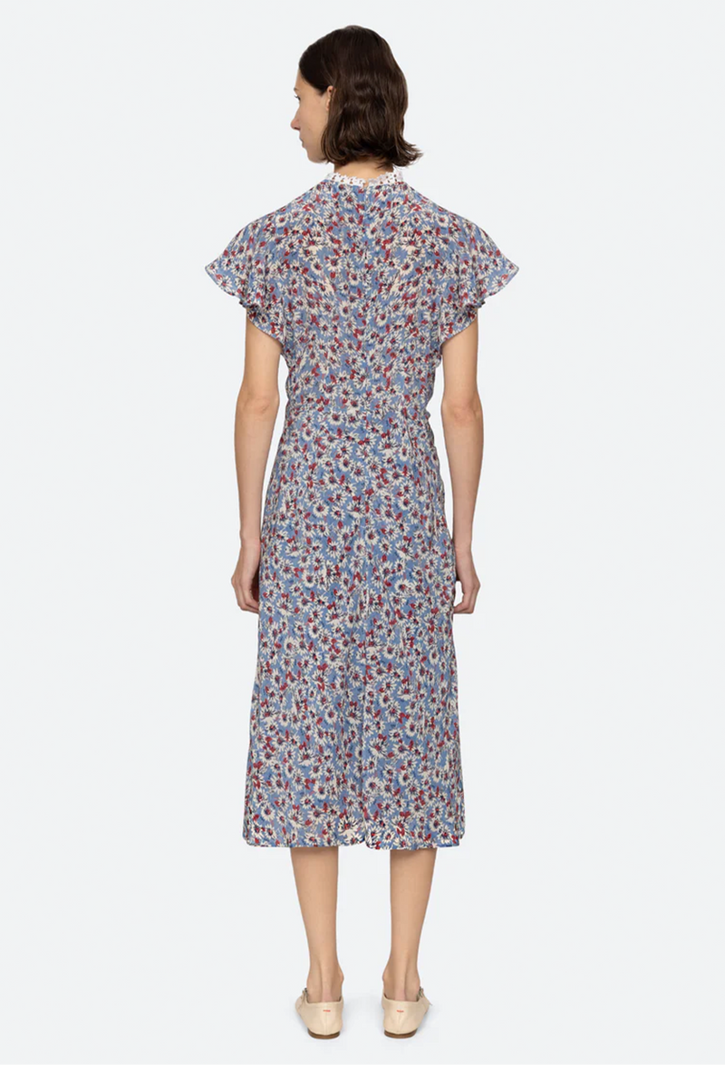 the back of a woman wearing a blue high neck midi dress with short flutter sleeves and a white and red floral print. white background.