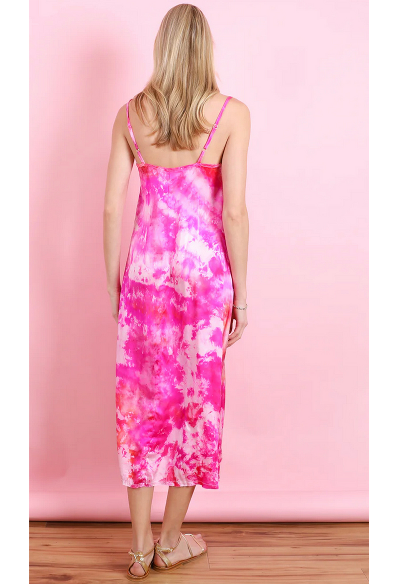 the back of a woman in front of a pink backdrop wearing a pink and white tie dyed midi slip dress.