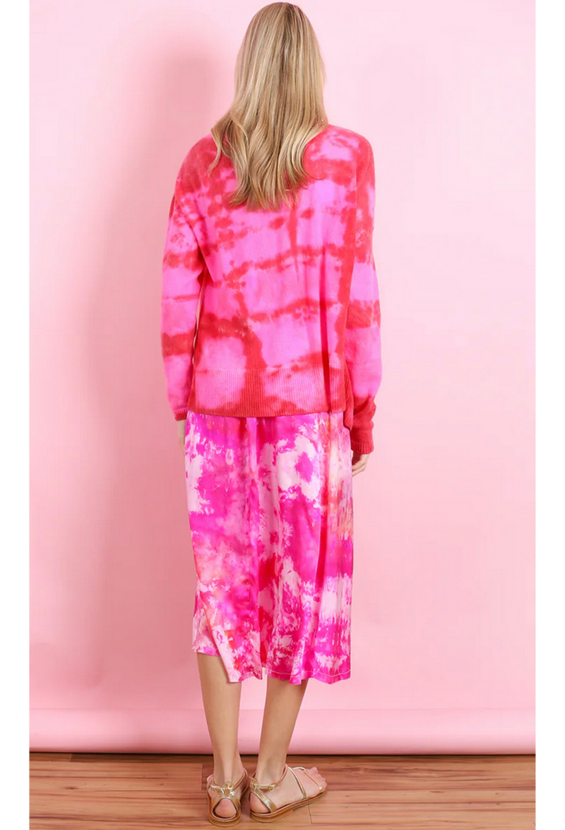the back of a woman in front of a pink backdrop wearing a pink and white tie dyed midi slip dress and a red and pink tie dyed cardigan.
