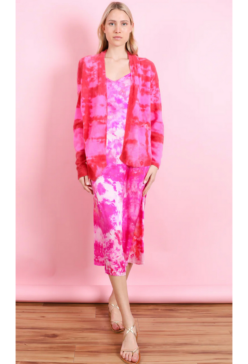 a woman in front of a pink backdrop wearing a pink and white tie dyed midi slip dress and a red and pink tie dyed open cardigan with two front pockets.