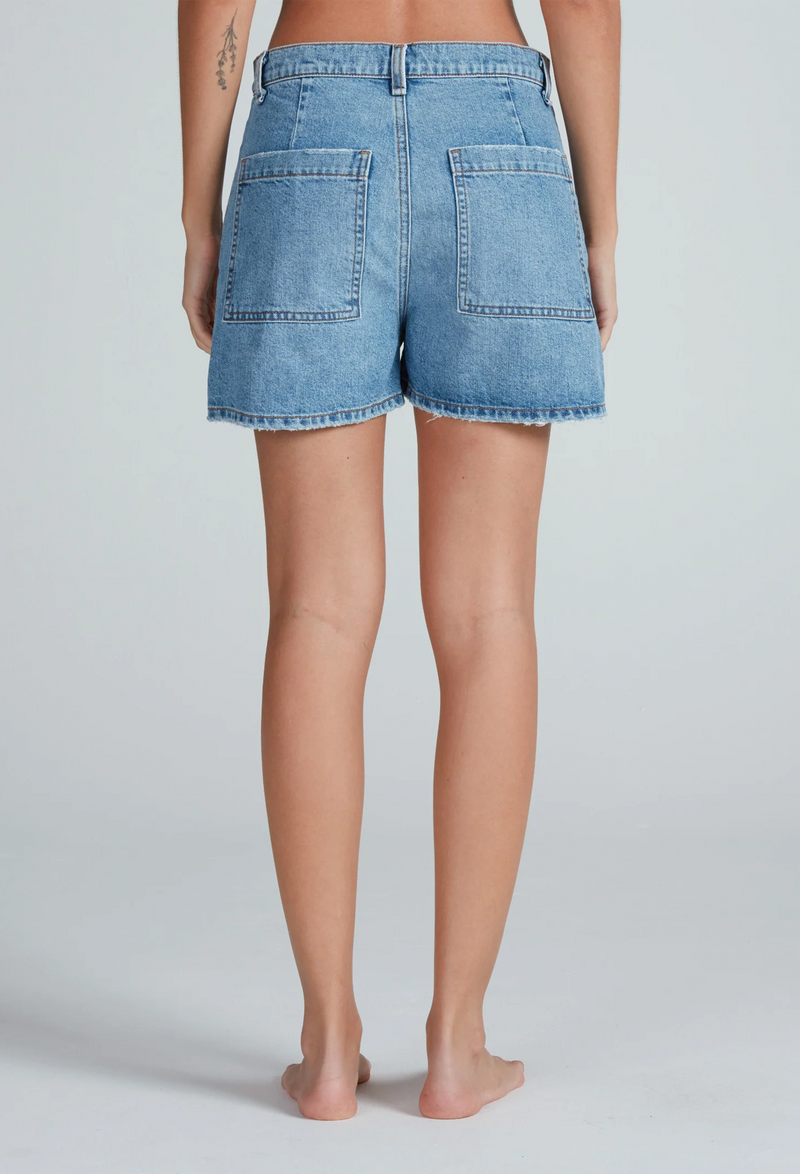 the back of a woman wearing light denim shorts with two large patch pockets. white background.
