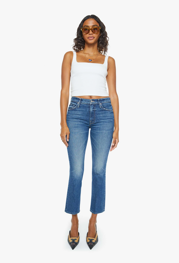 a woman wearing a white tank top with dark wash cropped jeans. white background.
