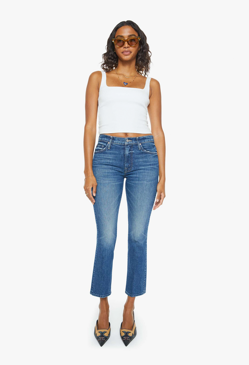 a woman wearing a white tank top with dark wash cropped jeans. white background.