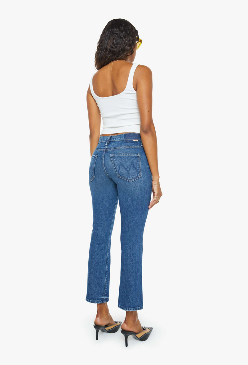 the back of a woman wearing a white tank top with dark wash cropped jeans. white background.