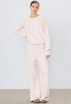 a woman wearing a light pink wide leg drawstring sweatpant and matching sweatshirt. white background.