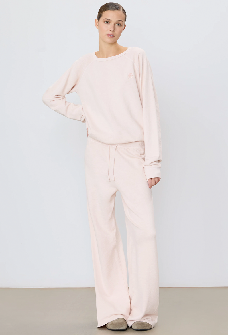 a woman wearing a light pink wide leg drawstring sweatpant and matching sweatshirt. white background.