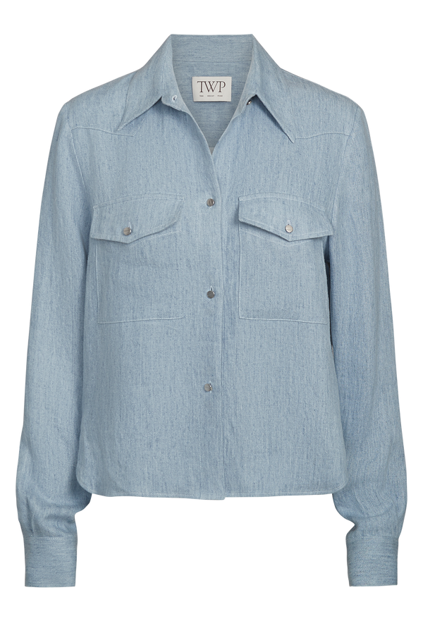 a light blue cropped button up work shirt with two chest flap pockets. transparent background.