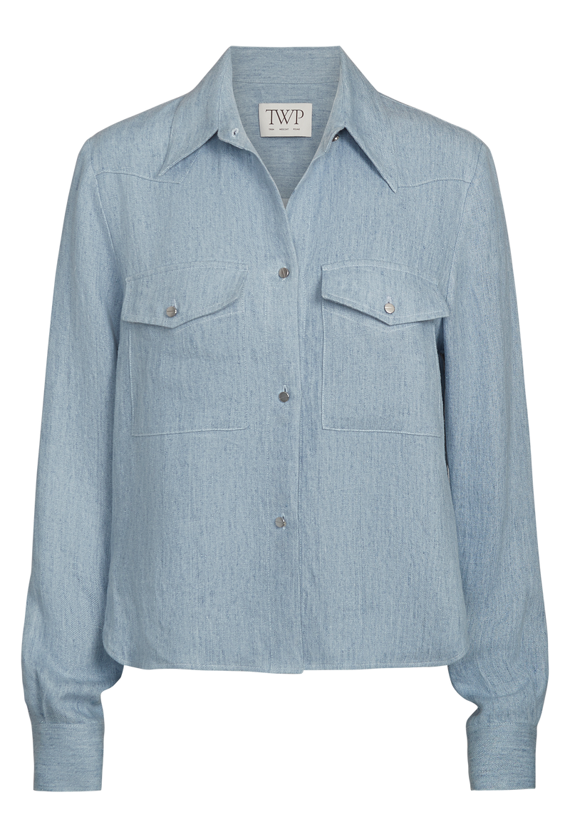 a light blue cropped button up work shirt with two chest flap pockets. transparent background.