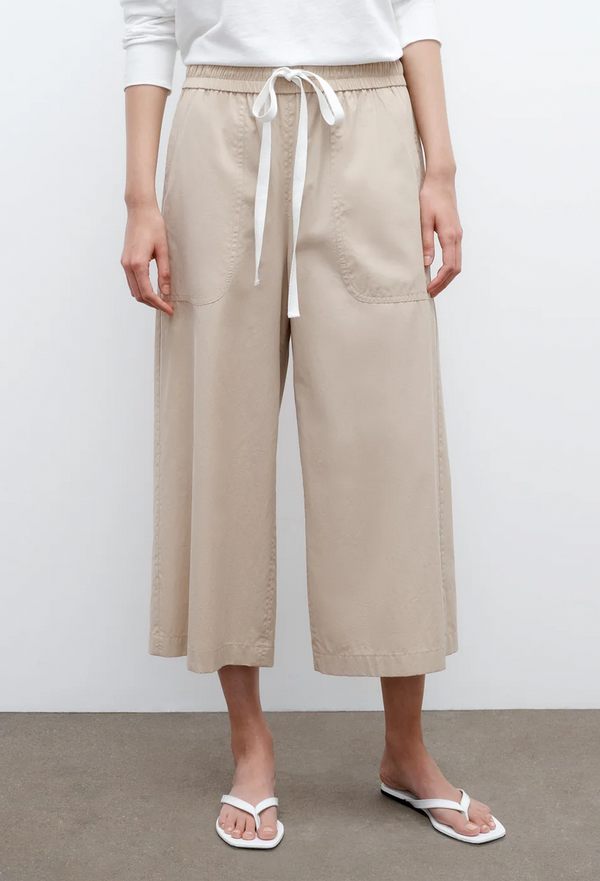 a model wearing a white top and cropped beige pants with two deep front pockets and a drawstring waistband. white background.