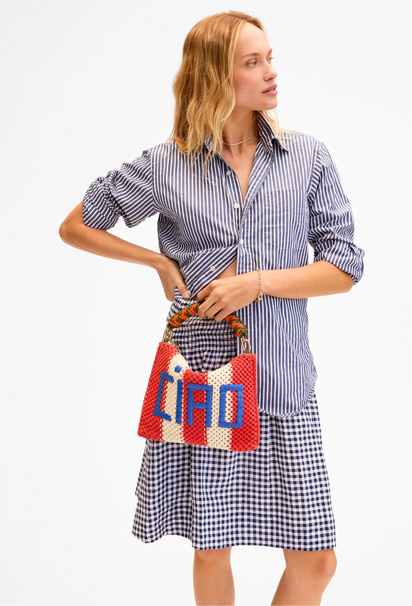 a model holding a flat clutch bag with thick red and white stripes and ciao written in blue embroidery. white background.