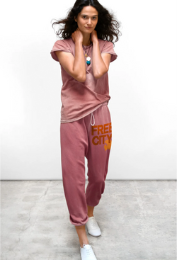 a model wearing a mauve t-shirt with mauve sweatpants with classic "FREECITY" print in deep orange and tonal light orange "FREECITYDOVE," covered elastic waist and pull drawcord. white background.