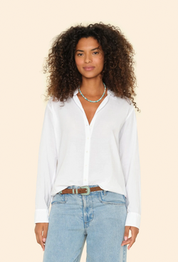 a model wearing jeans and a white long sleeve button down shirt tucked in. tan background.