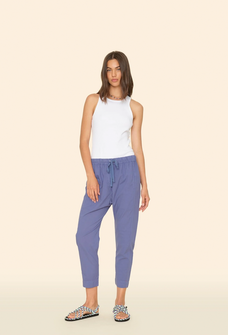 a model wearing a white tank top with indigo pull on drawstring pants. tan background.