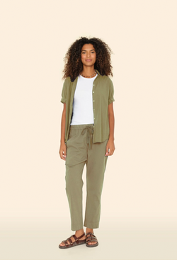 a model wearing a white top and open olive green button down shirt with matching olive green pull on drawstring pants. tan background.