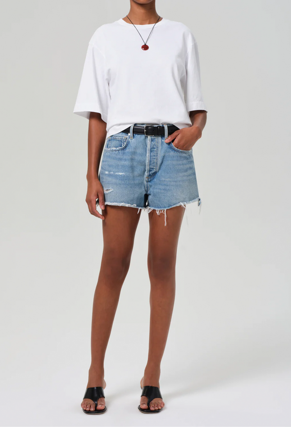 a model wearing a white t-shirt and frayed light wash denim shorts. white background.
