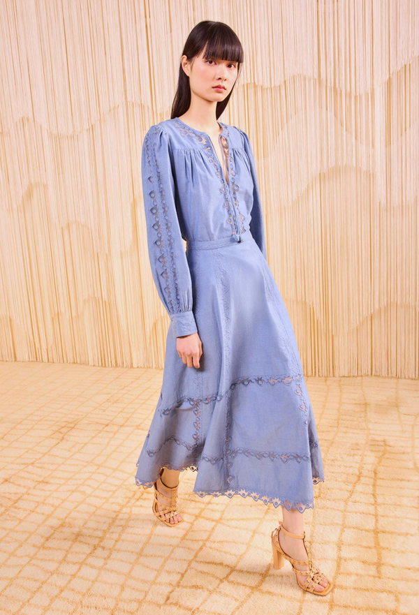 a model wearing an indigo long sleeve blouse and a matching midi skirt with tulle appliques. Beige background.