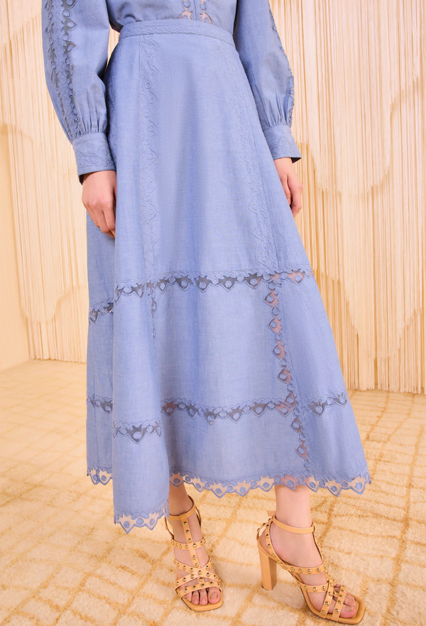 a model wearing an indigo long sleeve blouse and a matching midi skirt with tulle appliques. Beige background.