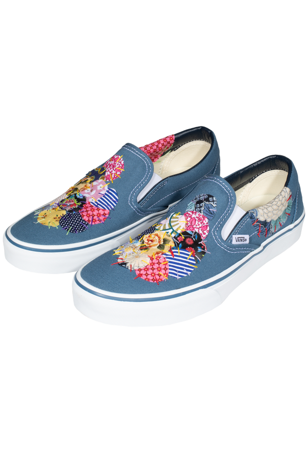 a pair of denim blue slip on vans with circular mulitcolored patterned patches of fabric stitched on. transparent background.