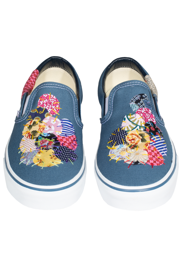 a pair of denim blue slip on vans with circular mulitcolored patterned patches of fabric stitched on. transparent background.