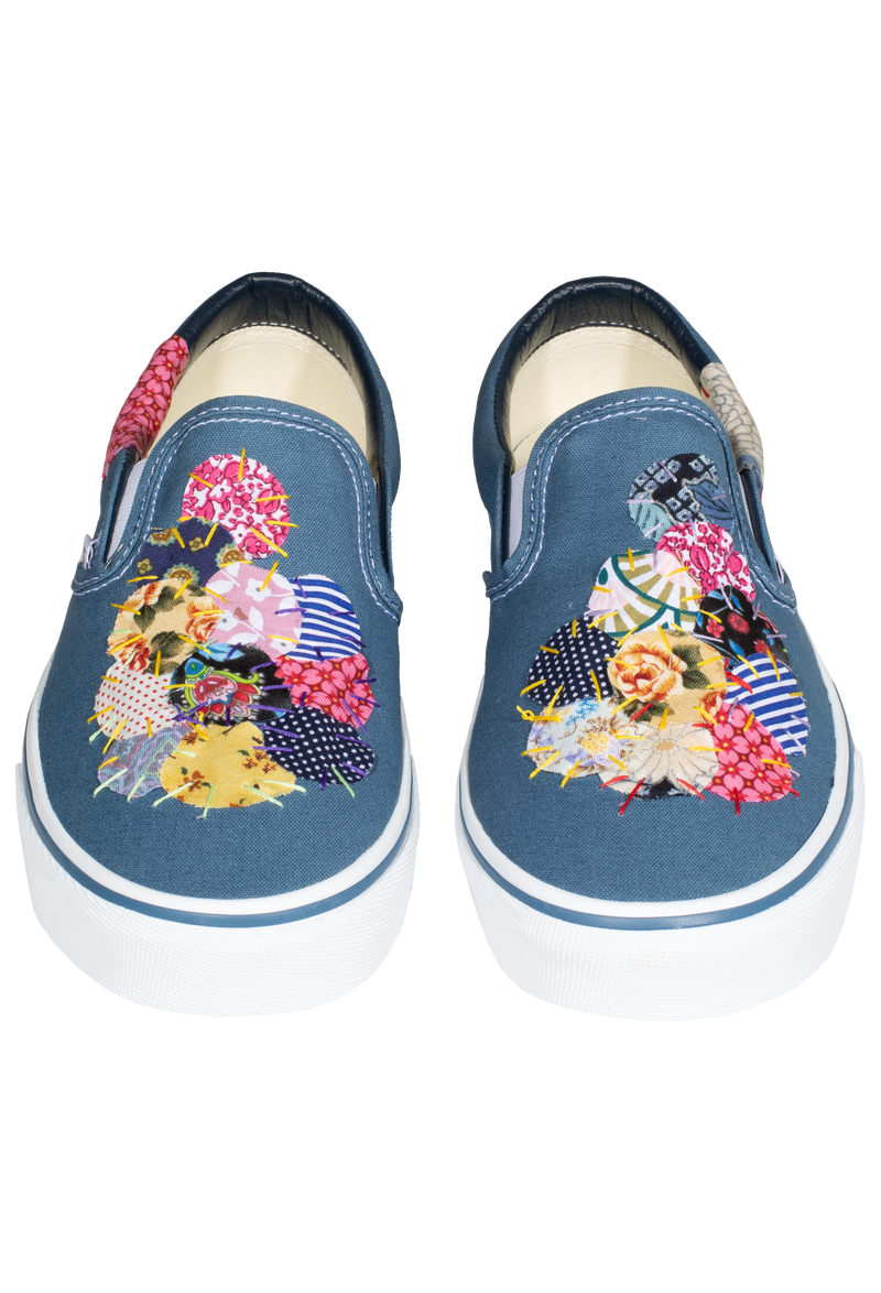 a pair of denim blue slip on vans with circular mulitcolored patterned patches of fabric stitched on. transparent background.