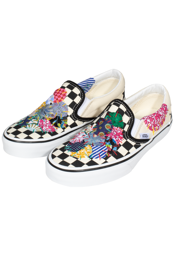 a pair of black and white checkered slip on vans with circular mulitcolored patterned patches of fabric stitched on. transparent background.