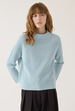 a model wearing a light blue funnel neck sweater with a ribbed textured knit. white background.