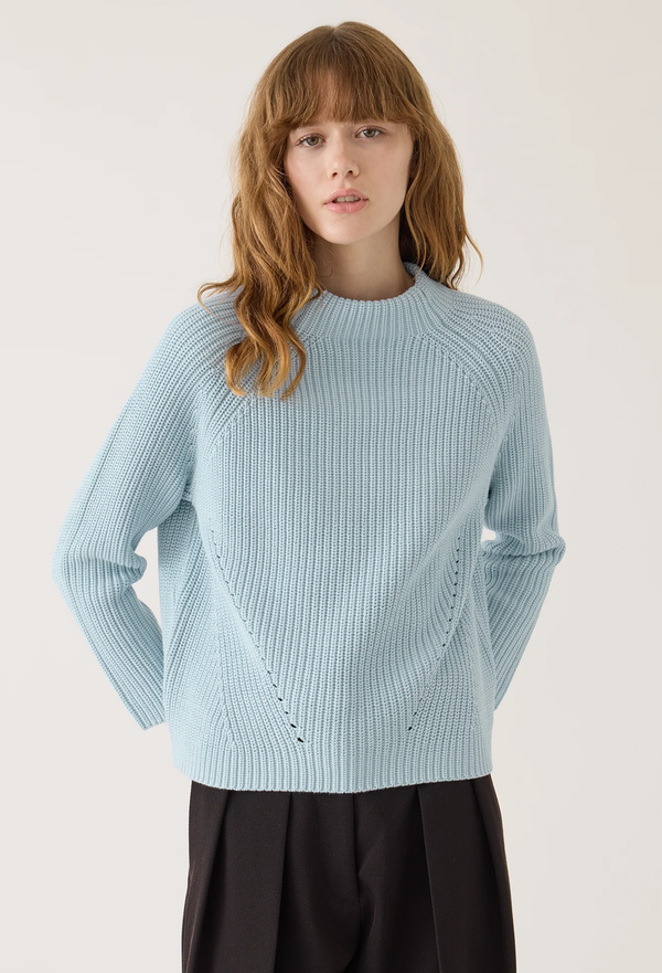 a model wearing a light blue funnel neck sweater with a ribbed textured knit. white background.