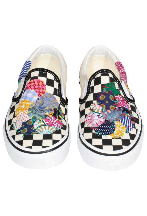 a pair of black and white checkered slip on vans with circular mulitcolored patterned patches of fabric stitched on. transparent background.