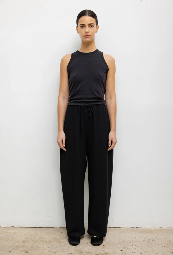 a model wearing a black tank top and black drawstring relaxed crepe pants. white background.